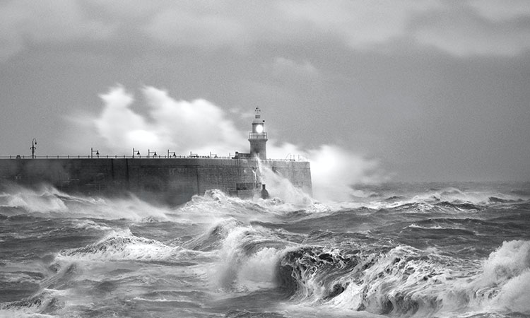 Pier and lighthouse in the ocean with waves crashing