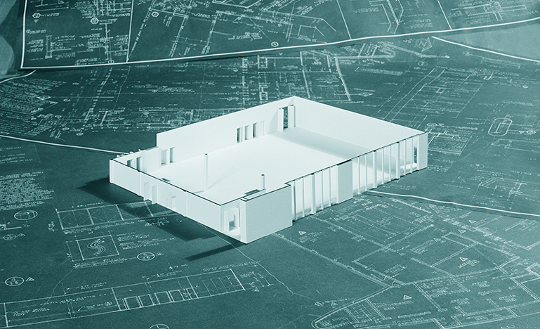 A model frame of a building sitting on a number of blueprints.