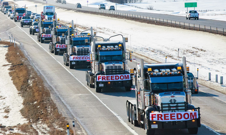 Shipping trucks driving down a highway with signs across each one with the word "freedom"