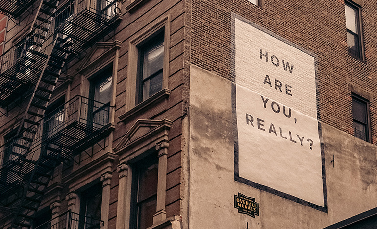 Large poster that reads "how are you, really" on the side of a brick building