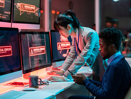 Two IT professionals looking at a set computer screens that have "CRITICAL ERROR" warnings.