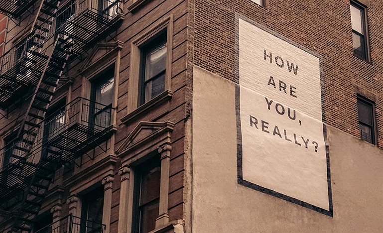 Large poster that reads "how are you, really" on the side of a brick building