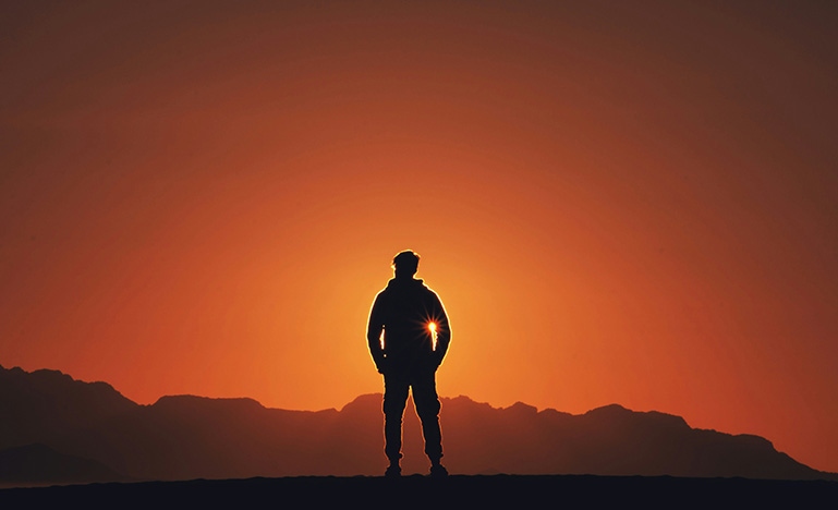 A person standing in silhouette in front of the setting sun.