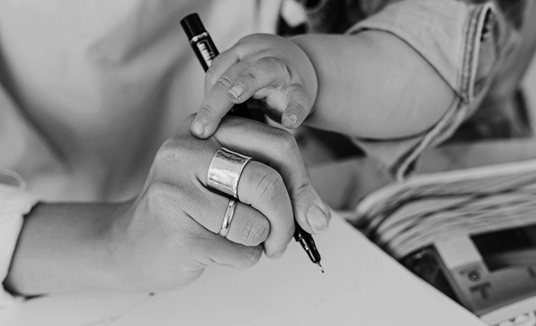 A parent holding their child in their arms while trying to write on a notepad.