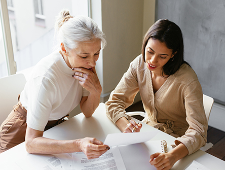 Two women seated at a table reviewing paperwork together. 