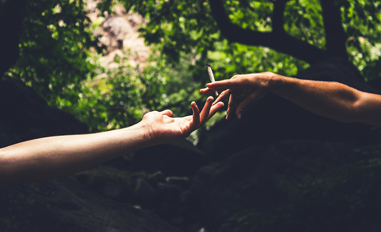 Two people in the forest passing a marijuana cigarette