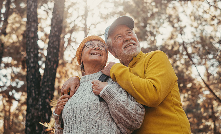 A senior couple embracing in a forest setting.