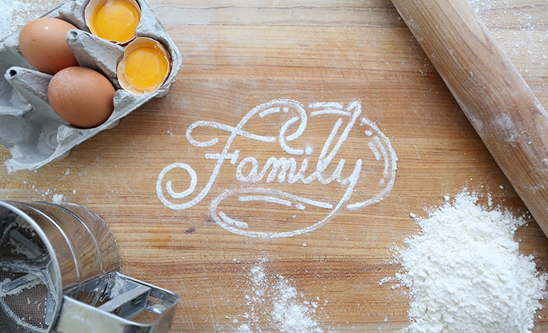 "Family" written with flour on counter with eggs and rolling pin