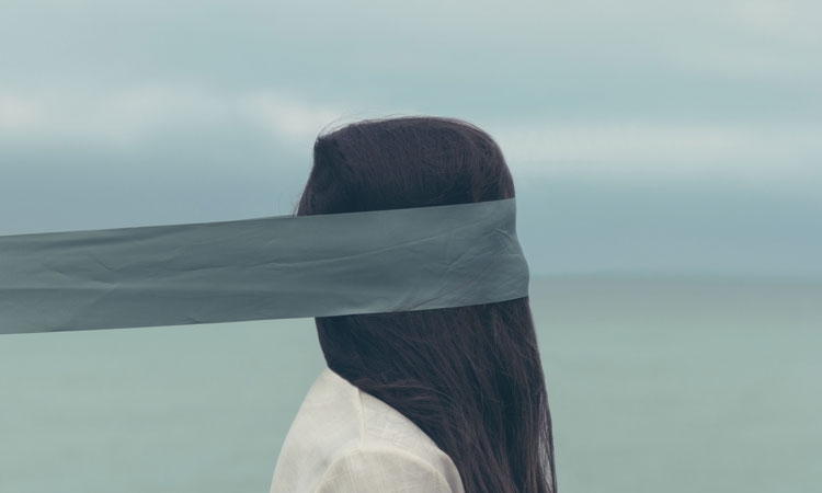 Person with long black hair and grey strip of fabric covering their face