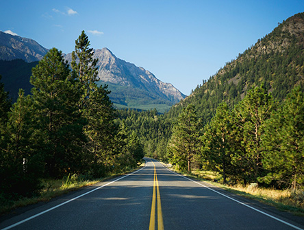 An open highway running through the mountains with forest on either side of the road.