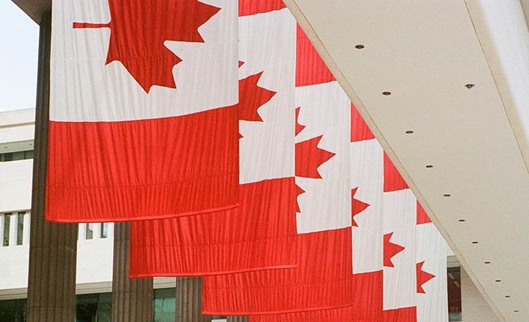Multiple Canadian flags hanging outside a government building.