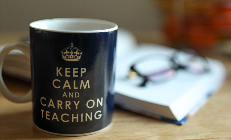 Mug with the phrase "Keep calm and carry on teaching" on desk with book and glasses