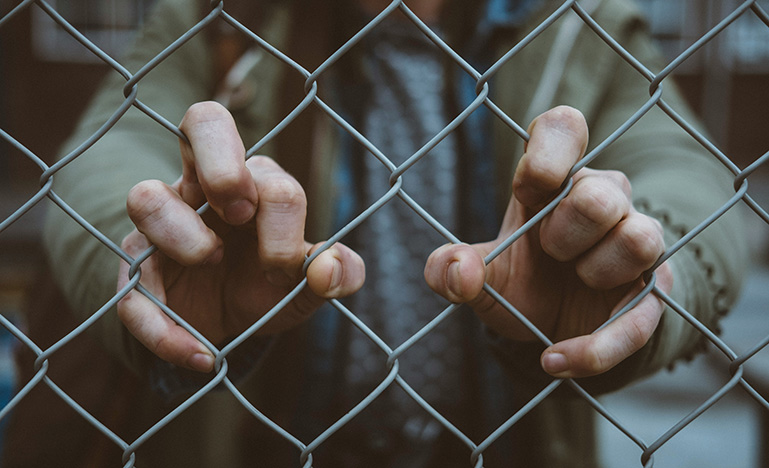 Close up of a person grabbing a chain link fence with both hands.