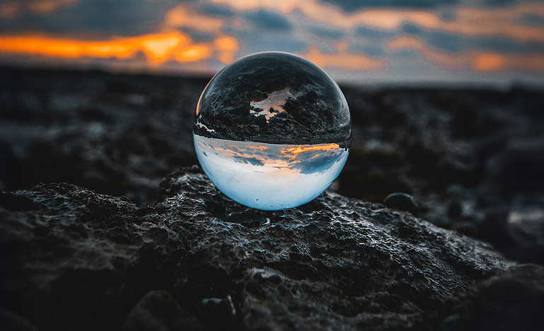A clear sphere sitting on the shore showing a reflection of the ocean behind it.