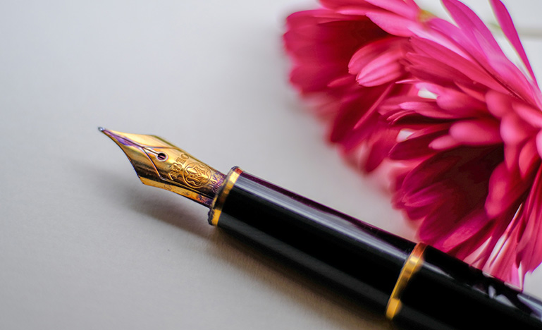 A fountain pen and a flower sitting on a desk.