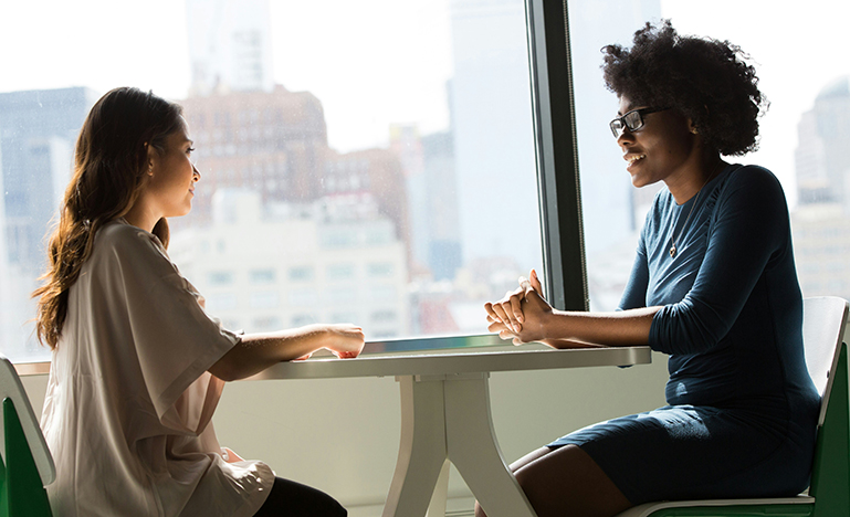 Two professional women sitting across a table from each other, deep in conversation.