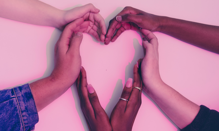 Six hands of diverse people forming a heart with a pink hue
