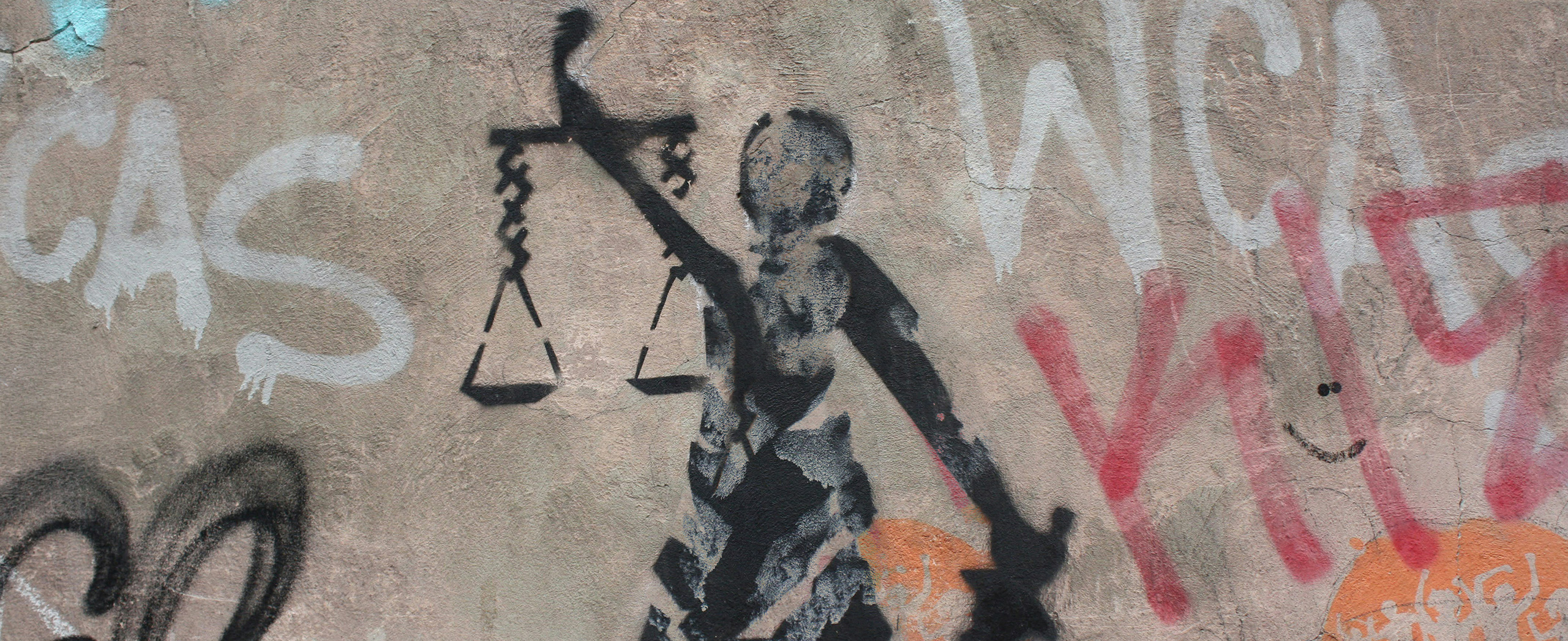 A spray-painted scales of justice surrounded by graffiti on a concrete wall.