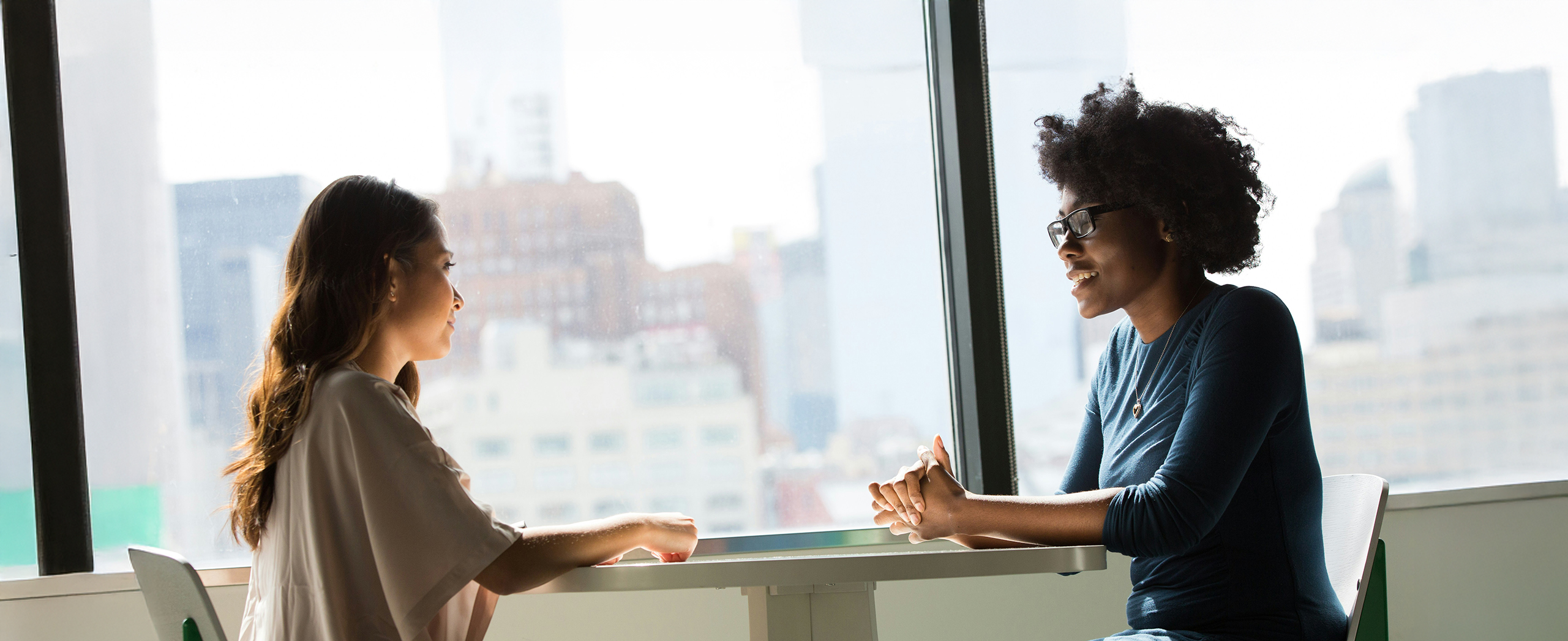 Two professional women sitting across a table from each other, deep in conversation.