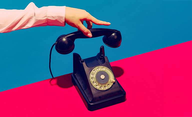 A hand holding the receiver of a vintage rotary phone. 