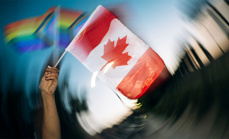 A person waving a Canadian flag and two inclusive Pride flags. 