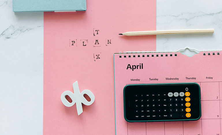 A calendar open to April, a calculator, pencil and a sign that reads "Tax Plan".