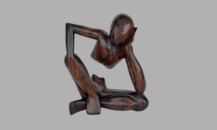 Wooden statue of a person sitting cross legged with its head resting on one hand