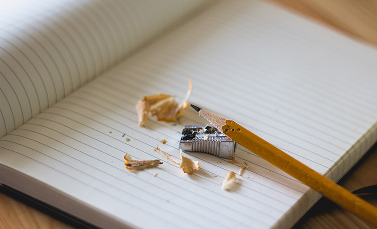 Freshly sharped pencil held above sharpener and shavings on open book