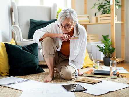 A senior person sitting on the floor surrounded by papers. 