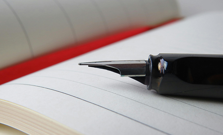 A fountain pen sitting on an open blank notebook.