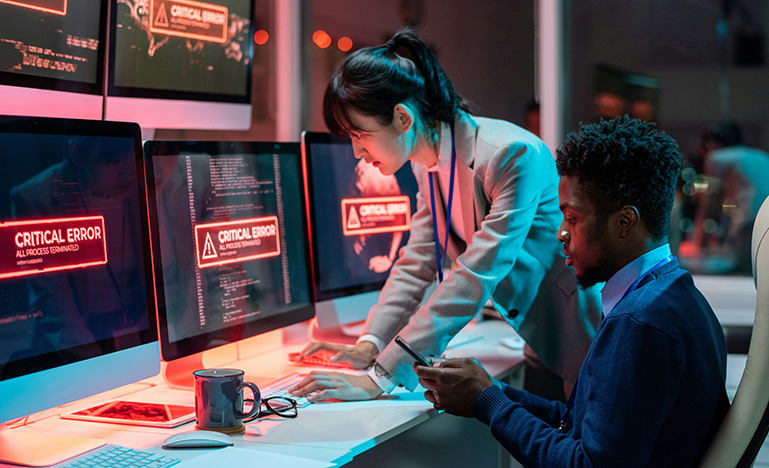 Two IT professionals looking at a set computer screens that have "CRITICAL ERROR" warnings.