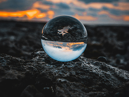 A clear sphere sitting on the shore showing a reflection of the ocean behind it.