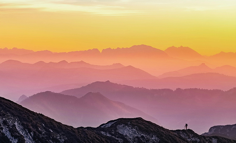 A lone hiker looks out over a vast mountain range.