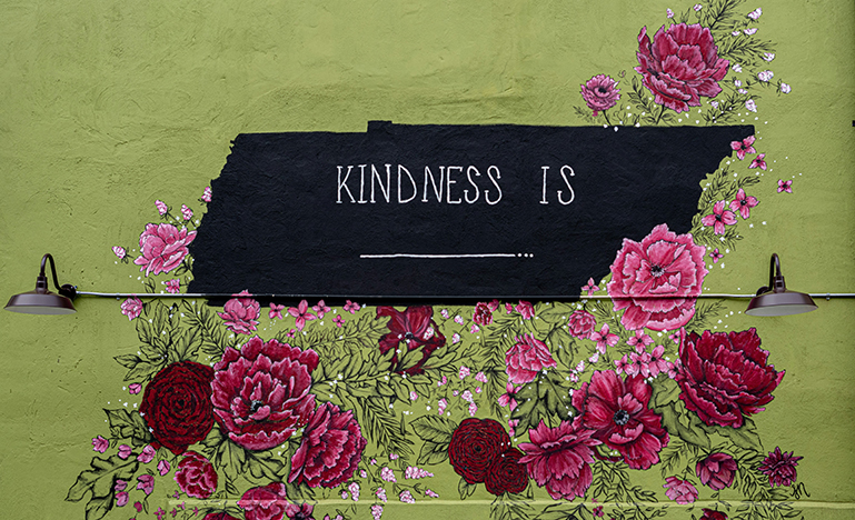 A sign on a wall that says "Kindness is _________" surrounded by flowers.