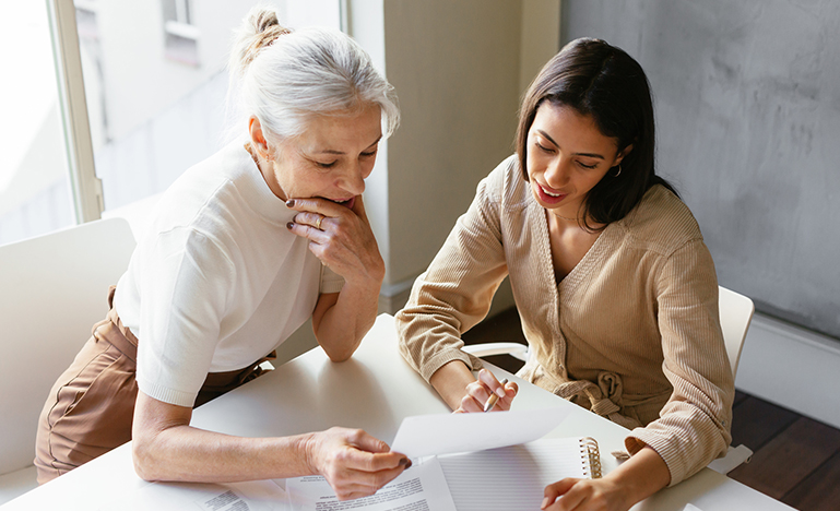 Two women seated at a table reviewing paperwork together. 