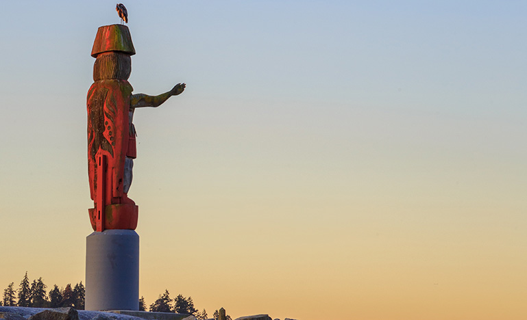 Red Indigenous statue with arm outstretched and a bird perched on the statue's head