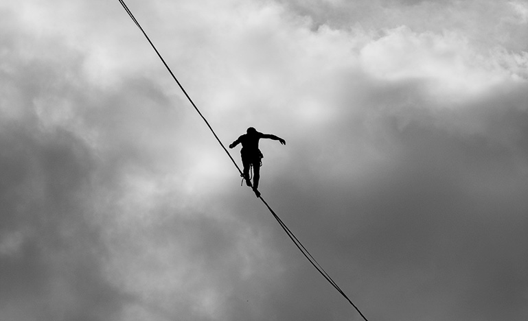 Person walking on tightrope in grey cloudy sky