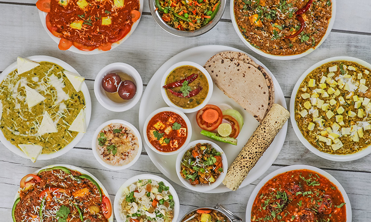 Indian food in white bowls and plates on white wooden table