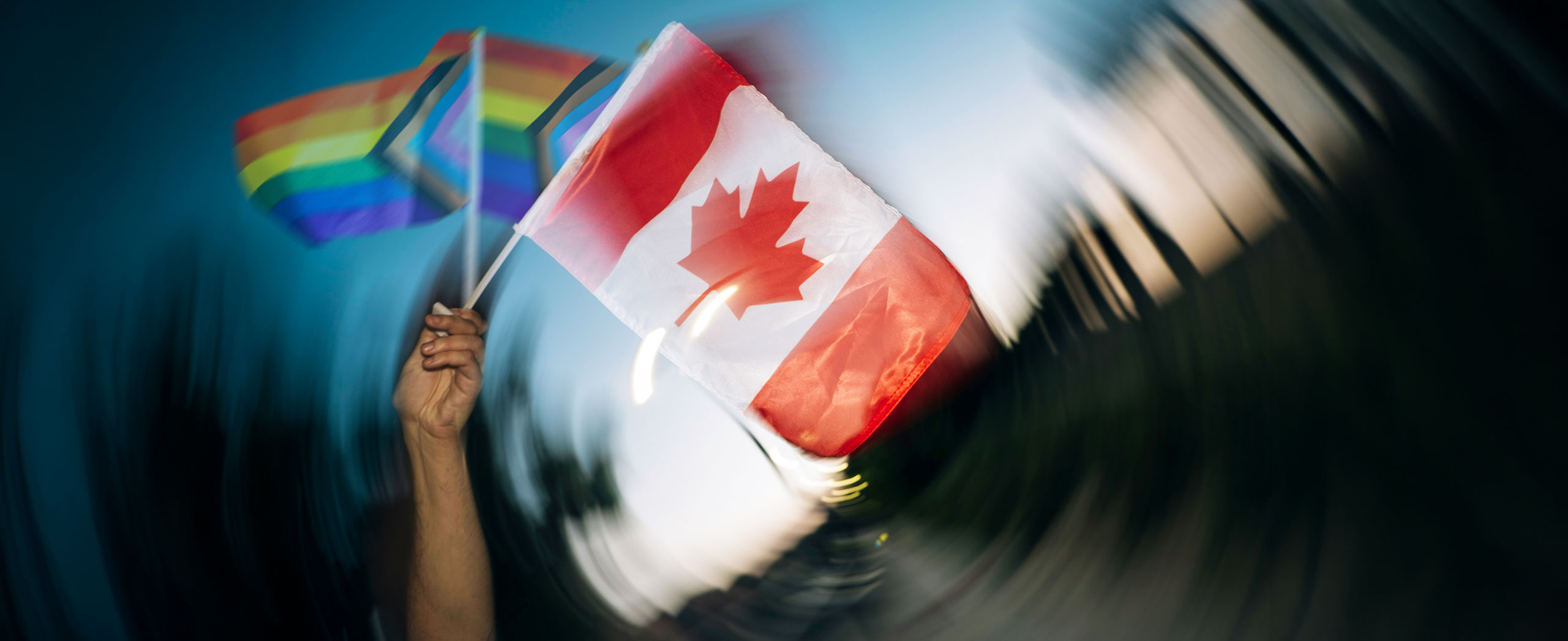A person waving a Canadian flag and two inclusive Pride flags. 