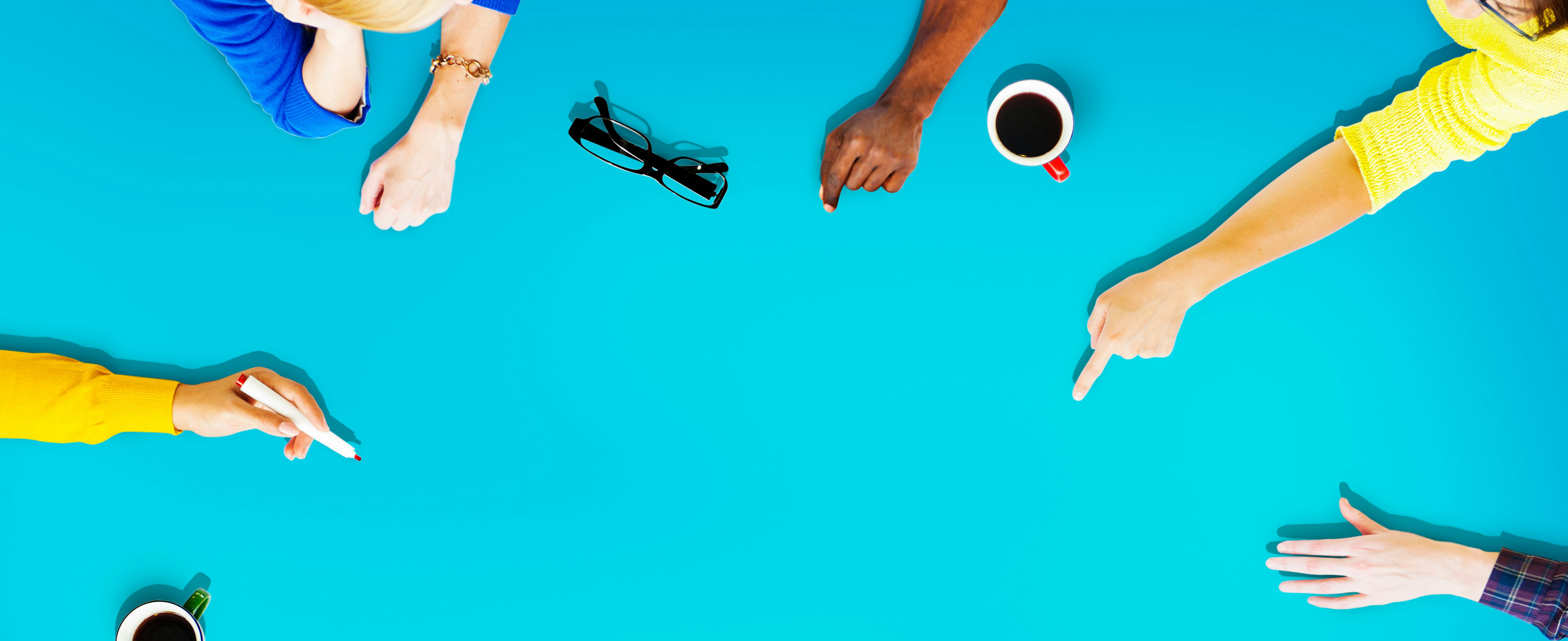 A circle of hands reaching into the middle of an empty table showing collaboration and participation. 