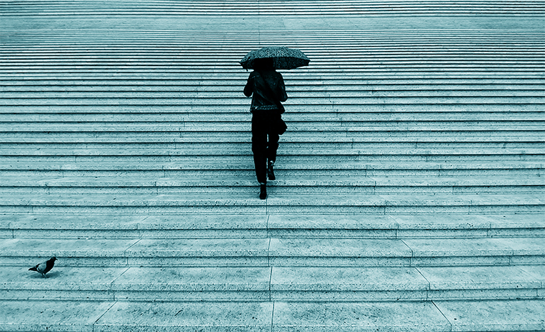 A professional walking up a large set of stone steps while holding an umbrella.