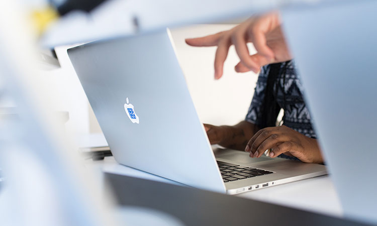 Hand pointing at a laptop screen while a different set of hands types on it