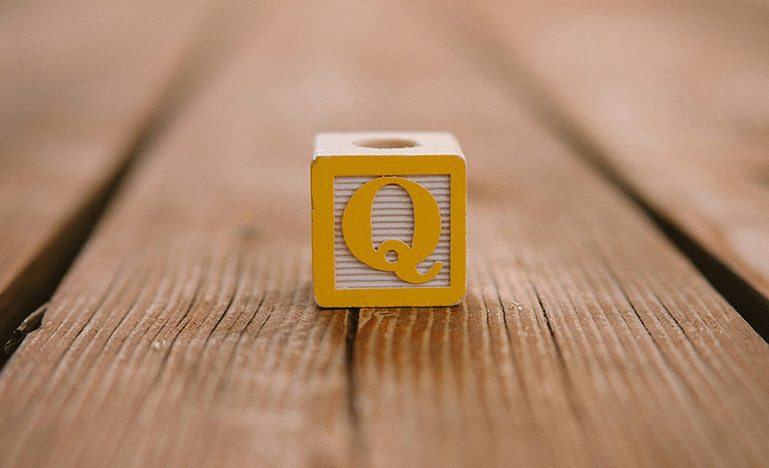 Wooden yellow block carved with the letter Q on a wooden deck