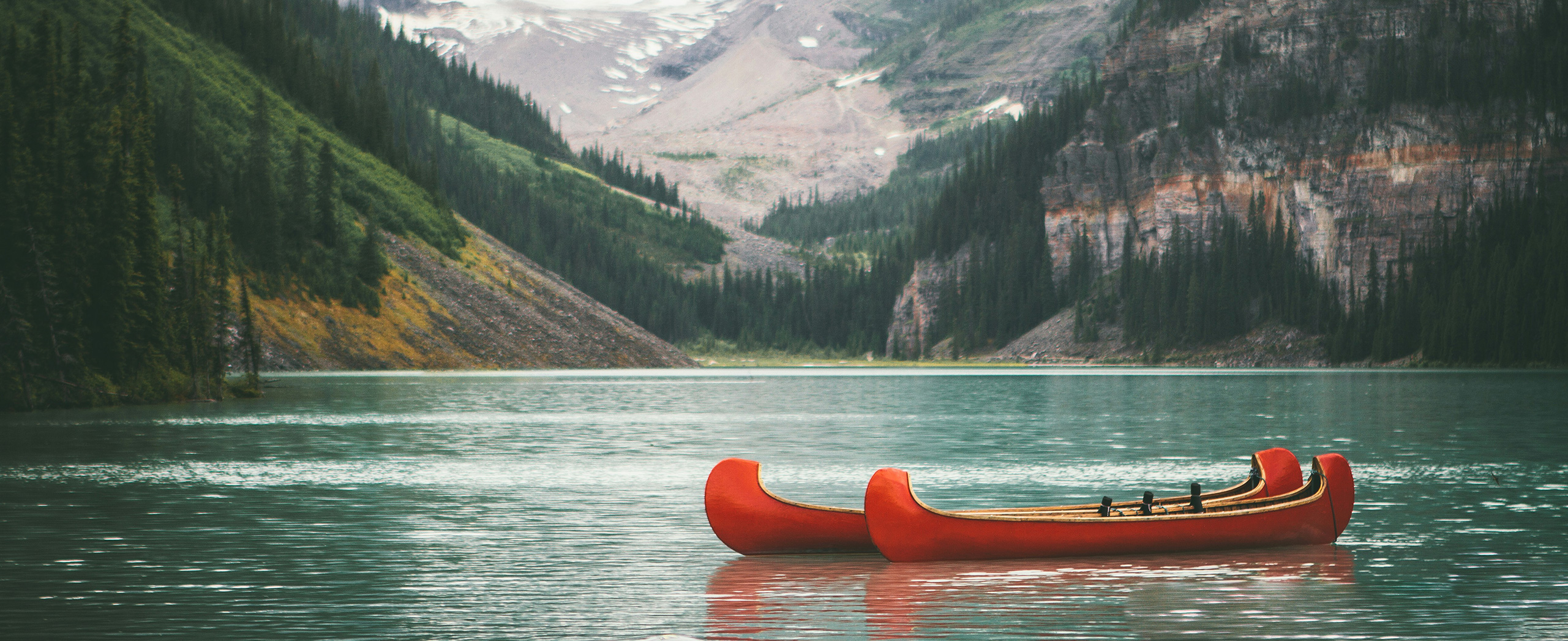 Two empty canoes on a pristine lake surrounded by mountains.