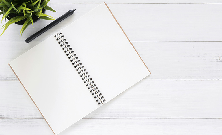 An open blank notebook and pen sitting on a wood desk.