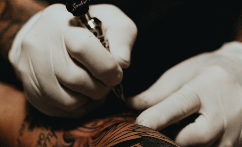 Hands wearing gloves tattooing person's arm