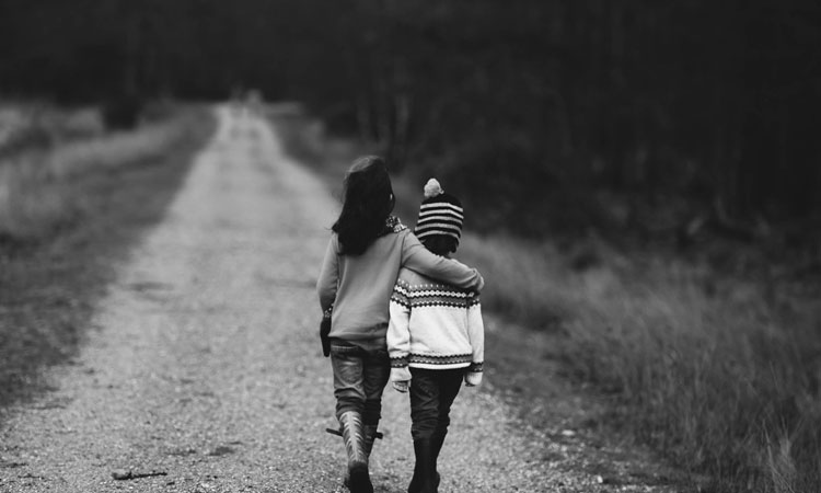 Two children walking arm in arm down a dirt path