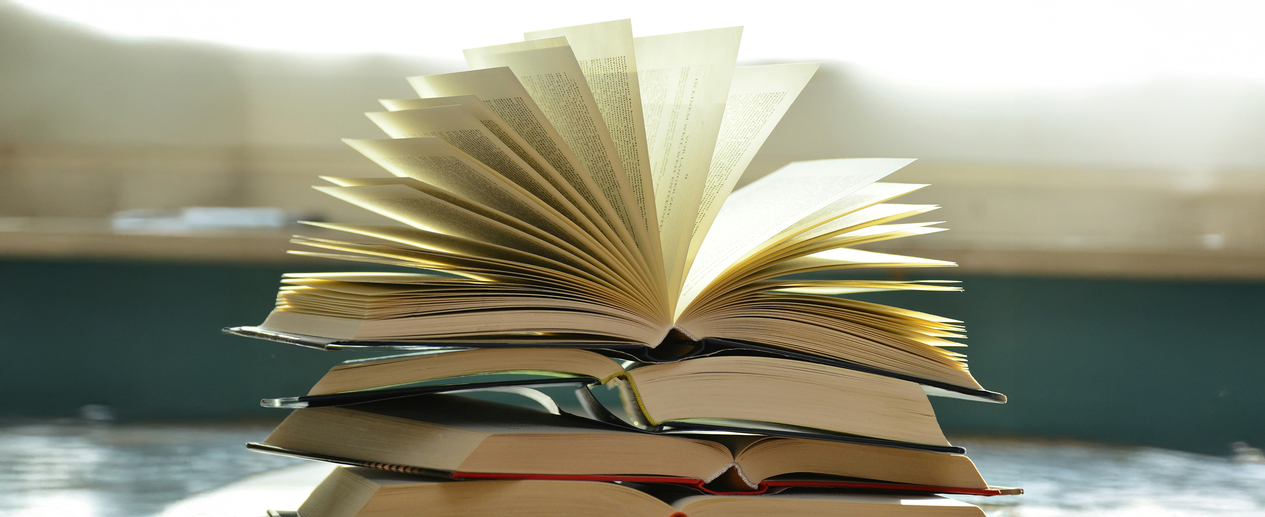 A stack of textbook with the top one open and the pages fanning out.