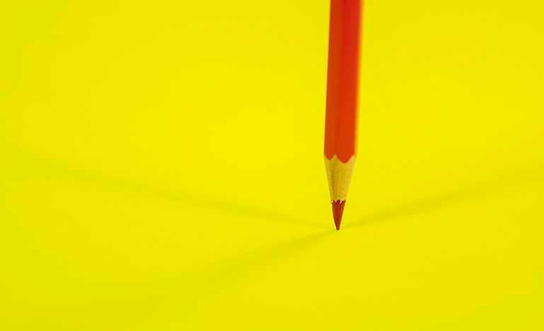 A red pencil on top of a bright yellow table