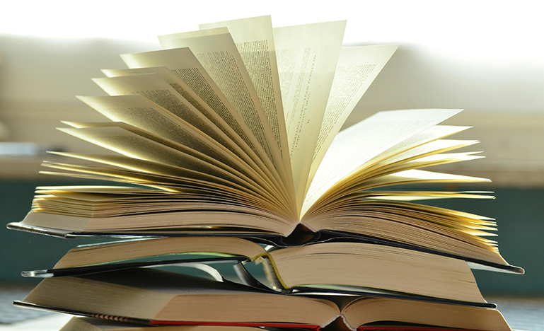 A stack of textbook with the top one open and the pages fanning out.